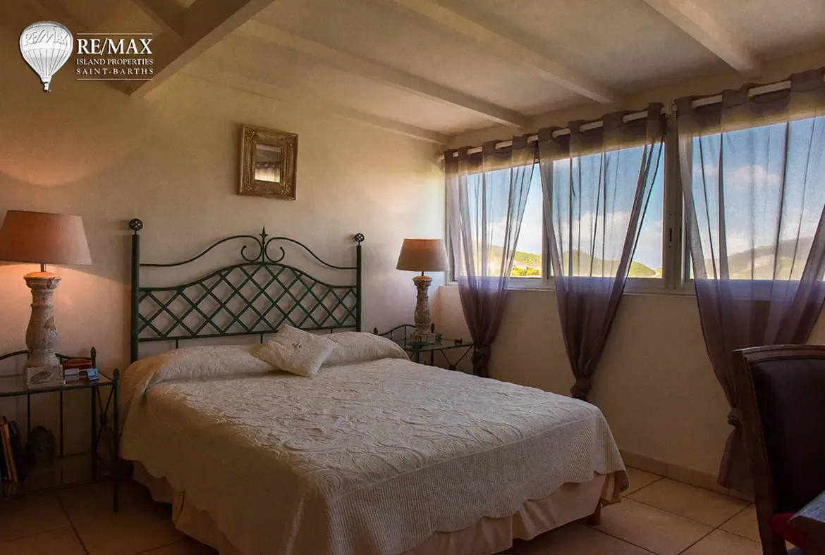 A charming bedroom with wrought-iron headboard and hillside views — restful island comfort with classic style.