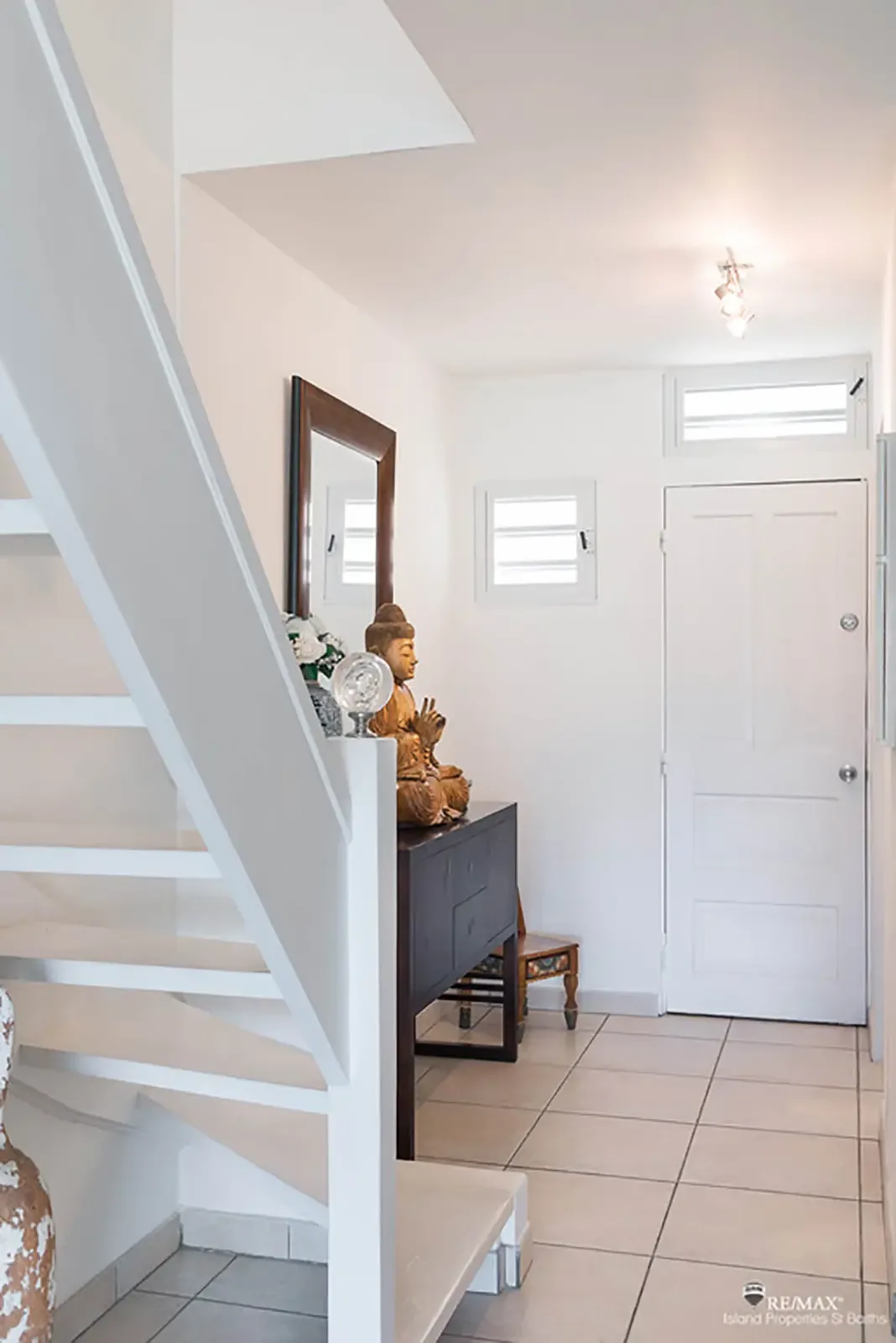 A bright entryway with open-riser staircase and Buddha statue — your welcoming entrance to Caribbean living.