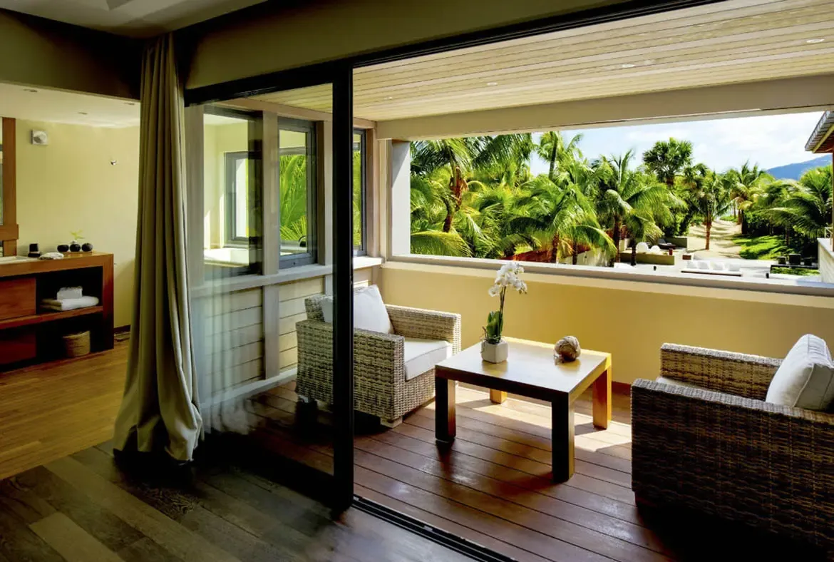 Two white-cushioned wicker chairs with an orchid-topped table face a lush tropical garden on this private terrace. Open doors connect the bedroom to the greenery just steps away.