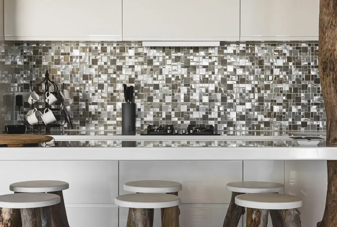 A sleek white kitchen island with gas stovetop and silver-brown mosaic backsplash gleams under soft natural light. Three rustic wooden stools with white seats line the island, while a tree trunk adds an organic accent—modern culinary elegance meets tropical warmth.