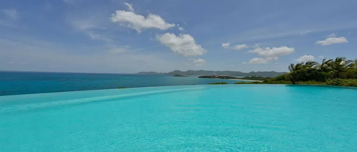 A turquoise infinity pool merges with the deep blue ocean, where lush green islands stretch across the horizon under a vast sky dotted with wispy clouds.
