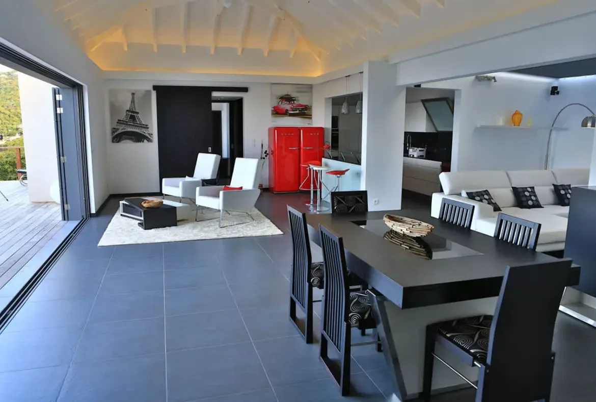 White armchairs with a red accent cushion face a black-and-white coffee table beneath an Eiffel Tower artwork. A dark dining table with patterned chairs leads to the vibrant red SMEG fridge and kitchen bar—open-concept living where every detail pops with personality.