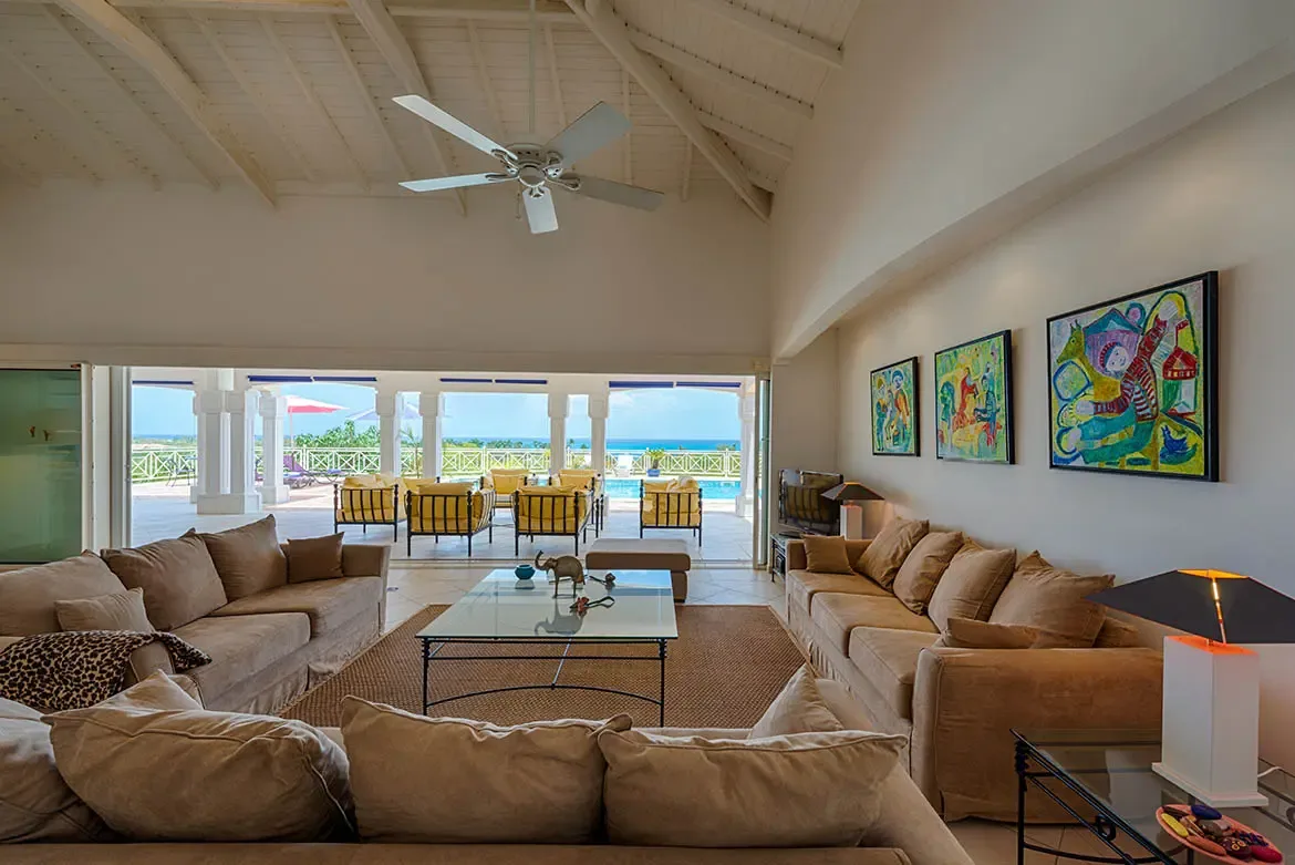 Three tan corduroy sofas and an ottoman circle a glass table on a sisal rug, where colorful abstract paintings and arched niches lead to a covered terrace above the ocean.