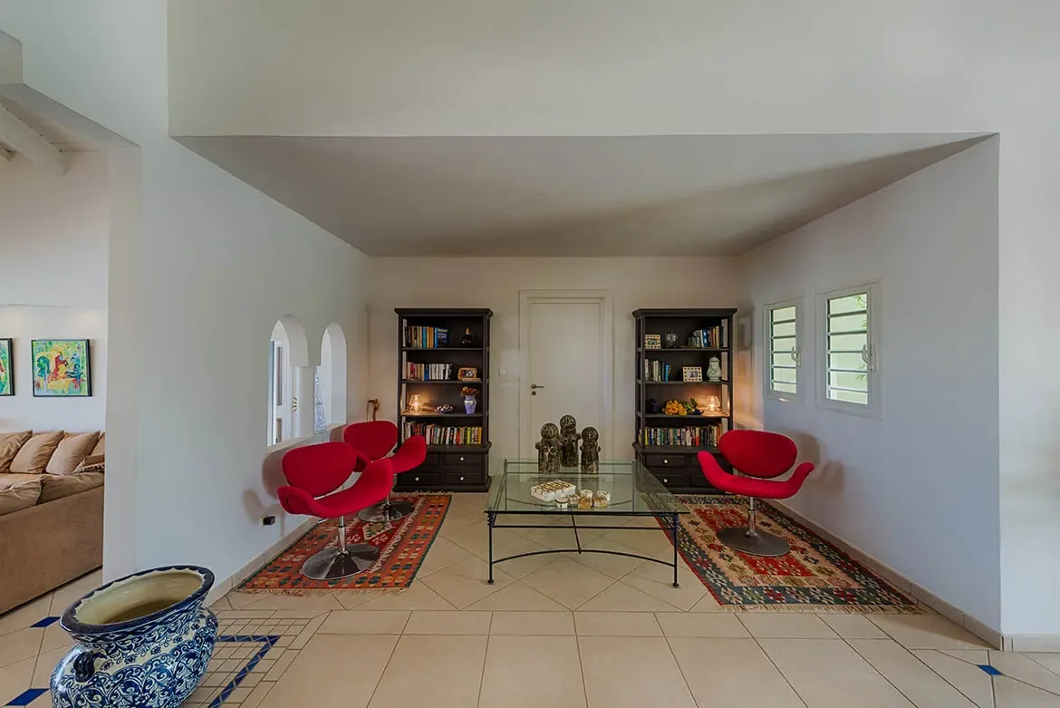 Three red tulip swivel chairs sit on patterned rugs beside glass tables and tall bookcases, where arched windows and abstract art warm the vaulted living space.