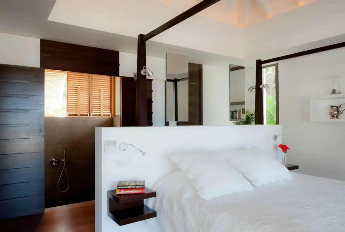 A white bed with plush pillows sits beside open glass doors, where a private infinity pool and lush tropical gardens create a serene bedroom retreat.