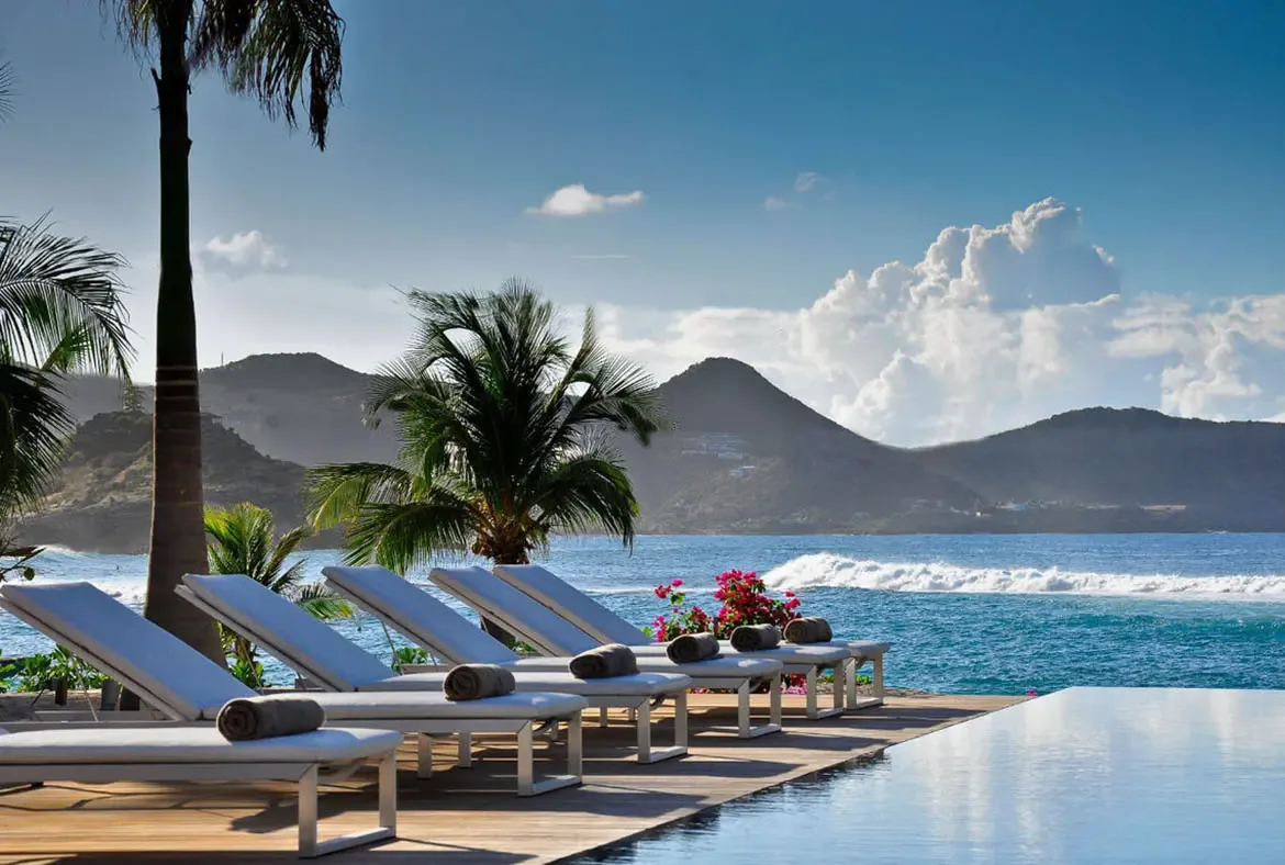 An infinity pool glows with blue underwater lights at night, where the villa interior illuminates warm white against a dark tropical hillside.