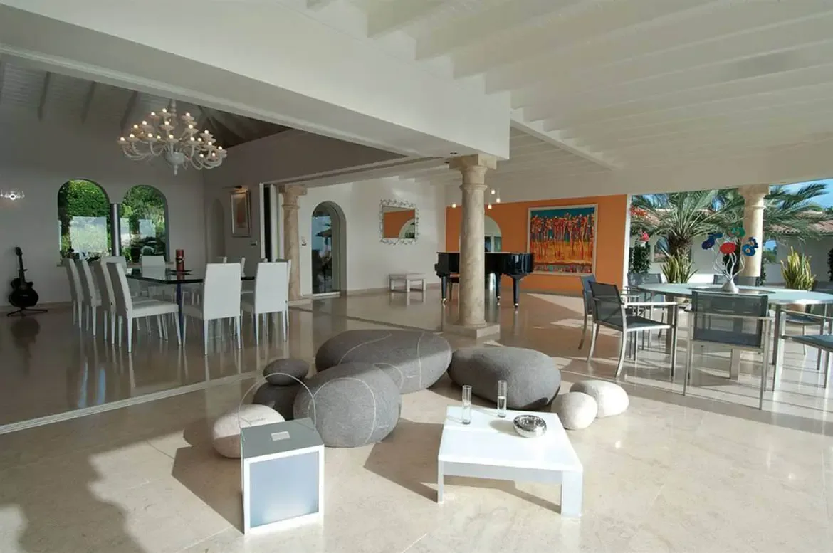 Orange accent pillows and a bamboo vase accent a white sectional sofa, where a grand piano sits beneath an orange wall with abstract art and pendant lights.