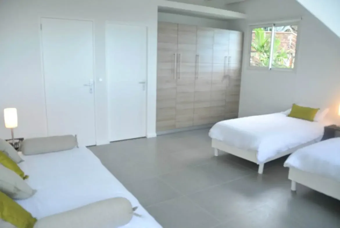 Bask in the tranquil ambiance of Villa Agave Azul's bright bedroom, where crisp white linens, sunlit tropical views, and modern comforts create the perfect sanctuary for rest and rejuvenation. Let the gentle St. Barths breeze and lush greenery visible through the window elevate your luxury escape.                                                                                                                                                                                                          +
 