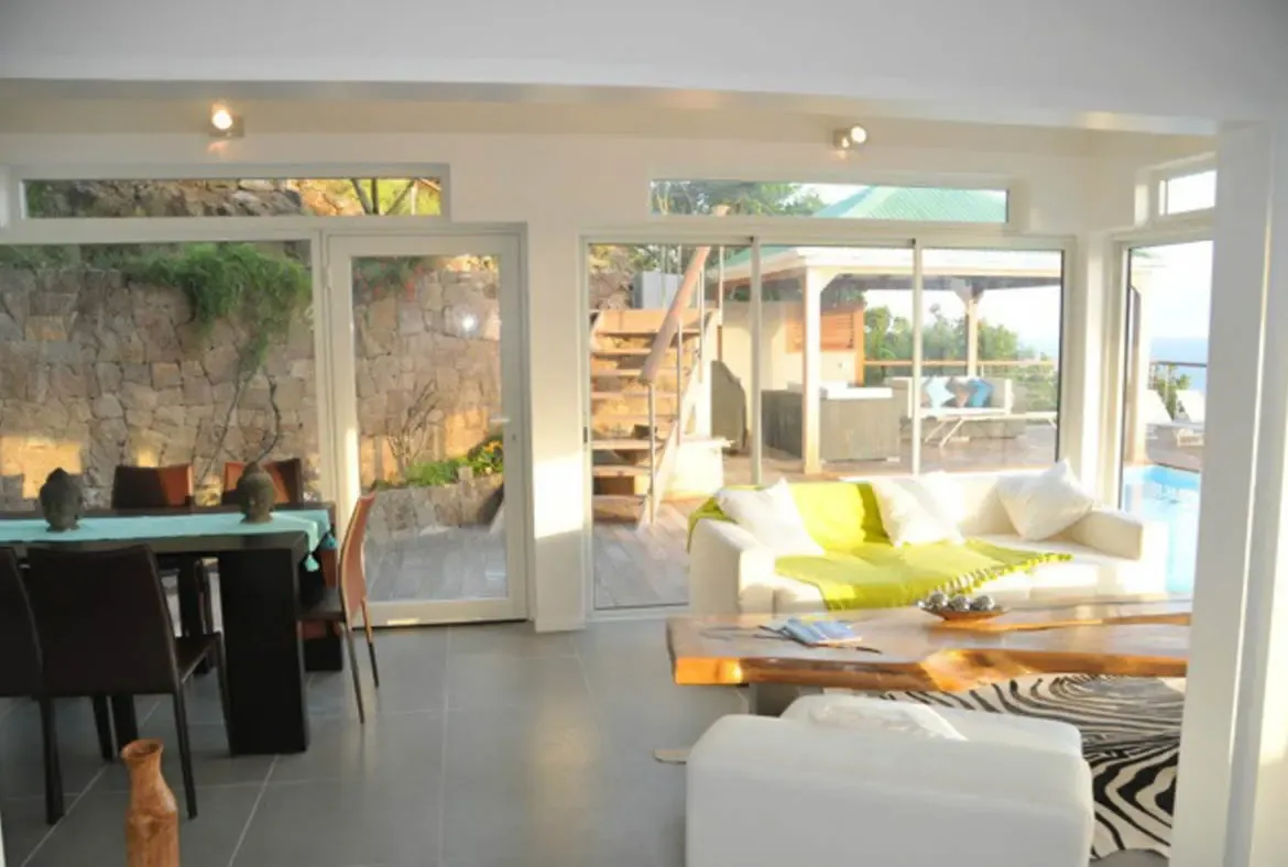 Experience the effortless elegance of indoor-outdoor living at Villa Agave Azul. This sun-drenched, open-plan sanctuary features a sophisticated blend of modern design and tropical warmth. Expansive glass walls blur the lines between the refined interior and the inviting pool deck, allowing the gentle Caribbean breeze to flow through the plush living and dining areas. It is the perfect setting for lingering breakfasts or chic evening cocktails as the sun sets over the St. Barths horizon.+
 