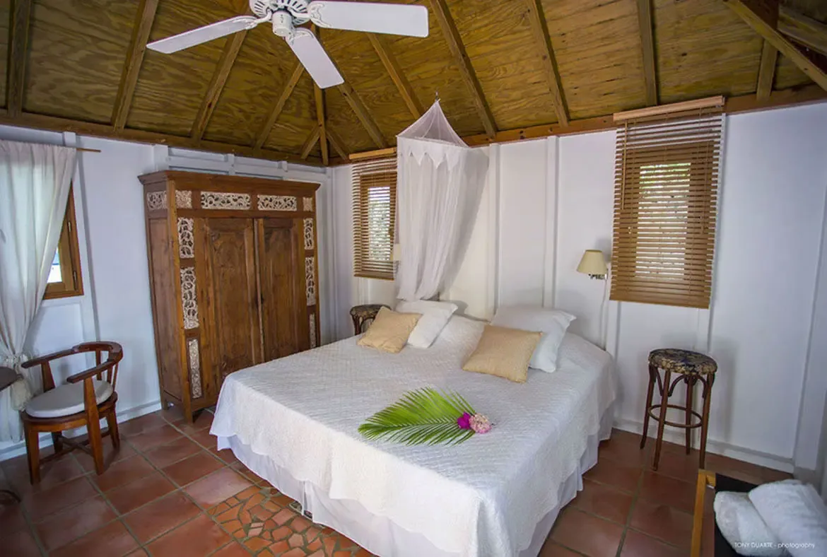 Drift into relaxation in this St. Barths sanctuary, where a handcrafted wooden ceiling and billowing mosquito net frame your peaceful escape. Wake to gentle light through bamboo blinds, surrounded by artisanal woodwork and tropical accents that embody island luxury.