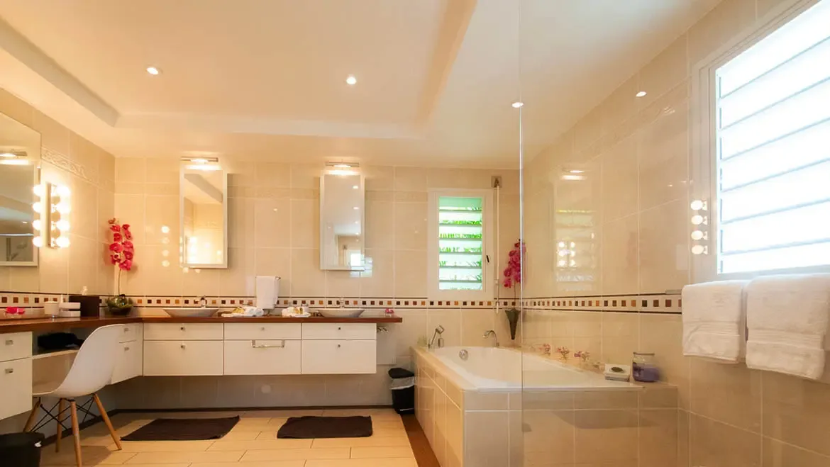 Indulge in the serene luxury of this expansive bathroom, where dual vanities and a sunlit soaking tub invite you to unwind. The warm, elegant design blends seamlessly with natural light streaming through louvered windows, creating a tranquil retreat after days spent exploring St. Barths.                                                                                                                                                                                                    +
 
