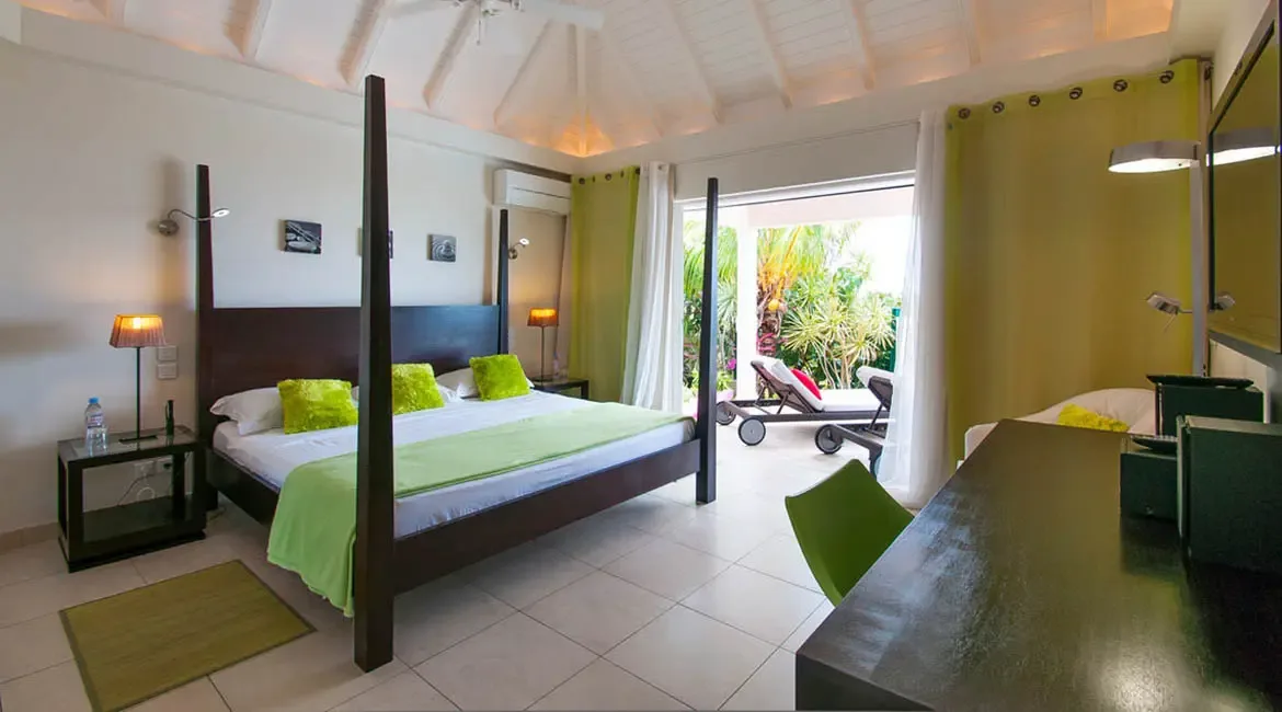 Drift into restful slumber on a four-poster bed adorned with vibrant green linens, as open doors reveal a private terrace nestled among tropical gardens. Savor the seamless blend of indoor comfort and outdoor serenity in this St. Barths sanctuary, where every detail invites relaxation under the Caribbean sun.                                                                                                                                                                       +
 