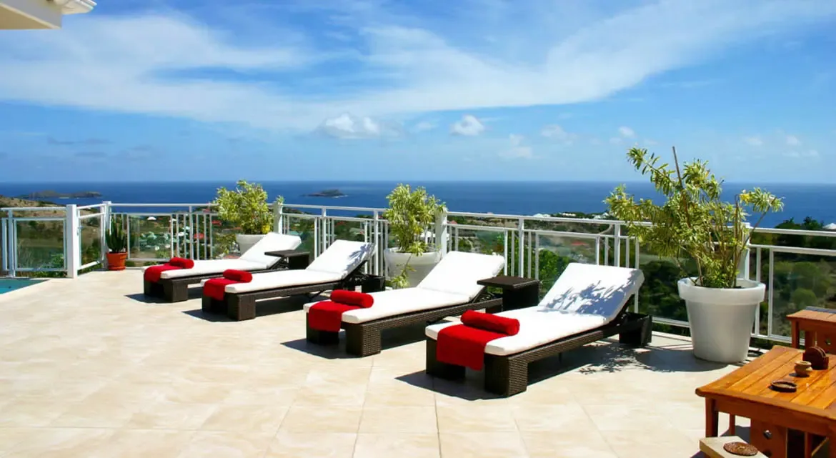 Bask in the tranquility of Villa Au Coeur du Rocher's sunlit terrace, where four plush lounge chairs draped in vibrant red towels invite you to unwind beneath the St. Barths sky. Savor uninterrupted ocean vistas stretching to distant islands, with gentle breezes and panoramic Caribbean horizons enhancing every moment of relaxation.                                                                                                                                                                  +
 