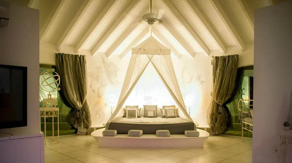Retreat into Villa Byzance's master bedroom, where a suspended canopy bed on a raised platform invites deep relaxation beneath a light-filled vaulted ceiling. Artistic wall murals and warm ambient lighting blend St. Barths' luxury with intimate serenity, crafting a dreamlike escape for discerning travelers.                                                                                                                                                                                            +
 