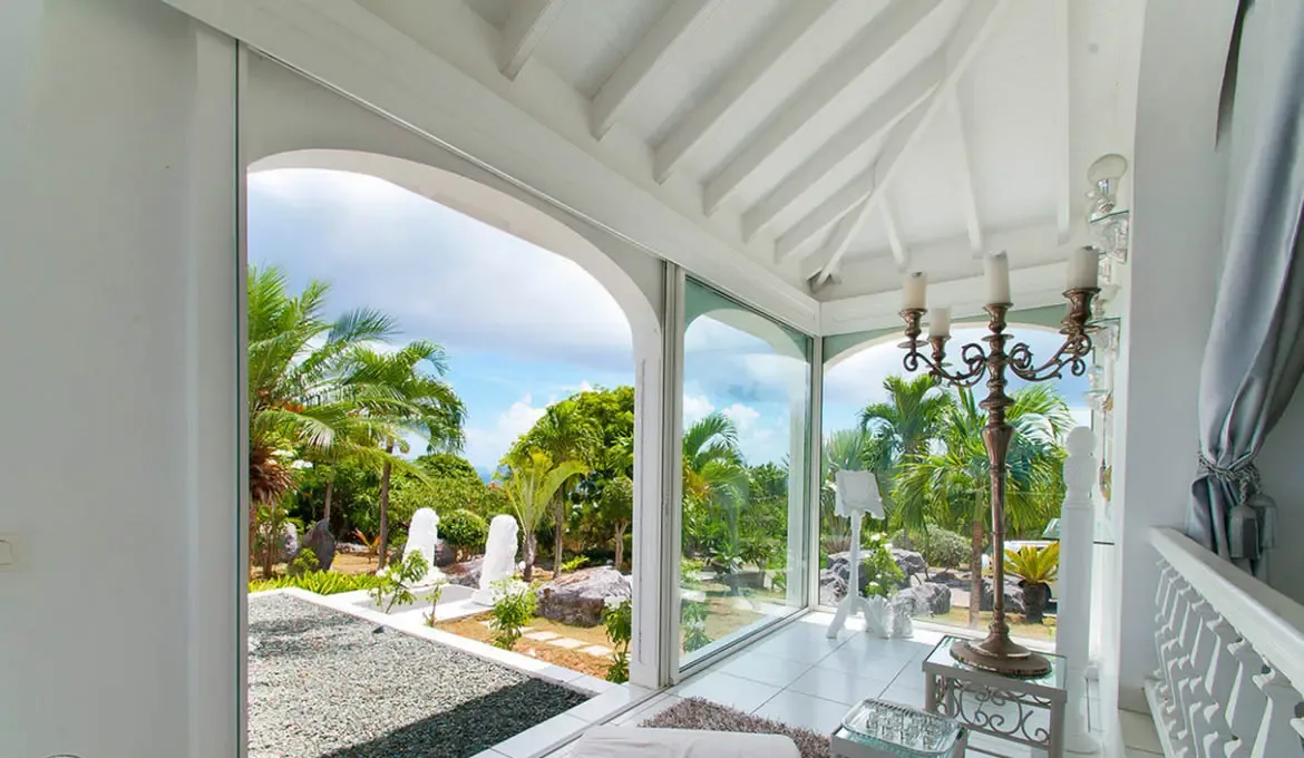 Step into the villa's light-filled living space, where elegant arches and glass doors seamlessly blend indoor luxury with the vibrant tropical garden beyond. Let the lush palm-fringed views and gentle island breeze create an atmosphere of effortless tranquility for your St. Barths escape.                                                                                                                                                                                                        +
 