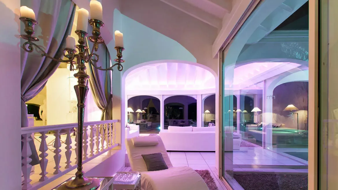 Unwind in Villa Byzance's luxuriously lit lounge, where a plush chaise and ornate candelabra set the stage for evening relaxation. Arched ceilings and glass doors blur the line between indoor elegance and the pool terrace's soft glow, capturing St. Barths' sophisticated ambiance.                                                                                                                                                                                                                                  +
 