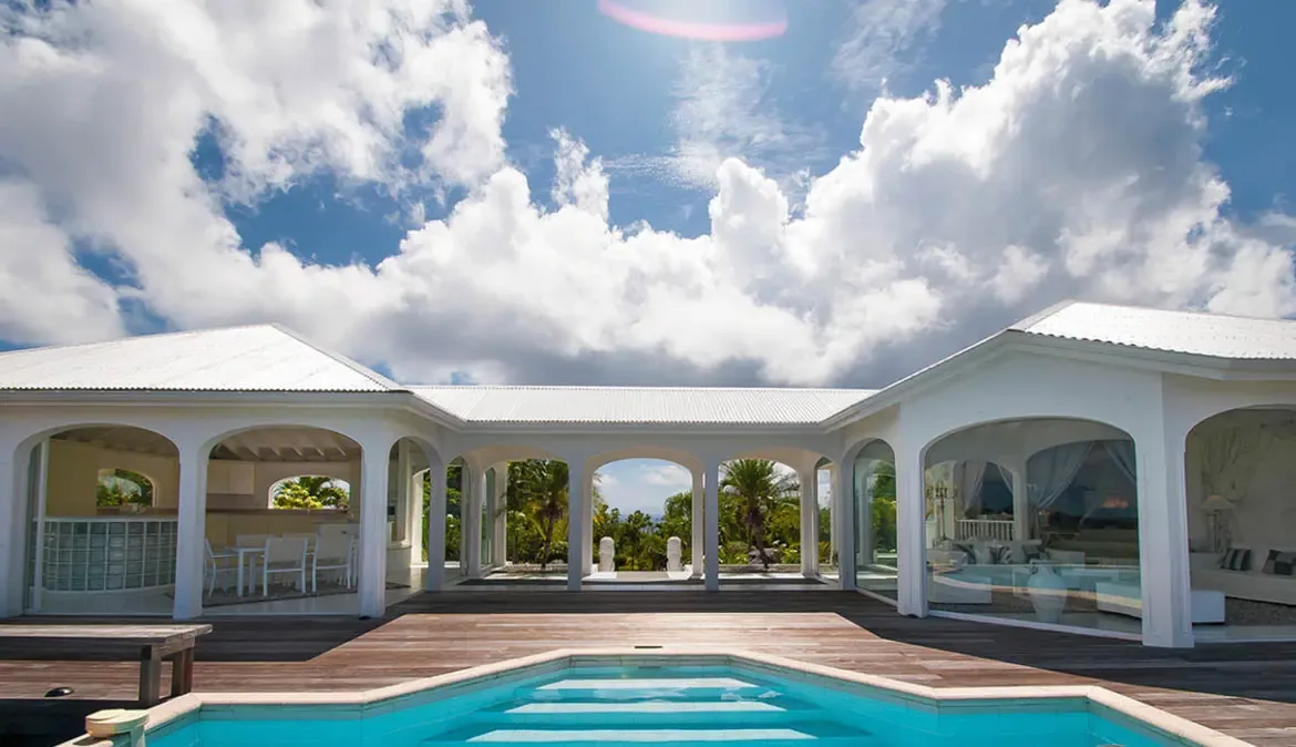 Bask in the luxury of Villa Byzance's open-air pool deck, where crystal-clear waters meet elegant white arches and sweeping views of lush tropical greenery. Let the gentle Caribbean breeze and endless blue skies transport you to a world of refined relaxation and effortless elegance.                                                                                                                                                                                                                                 +
 