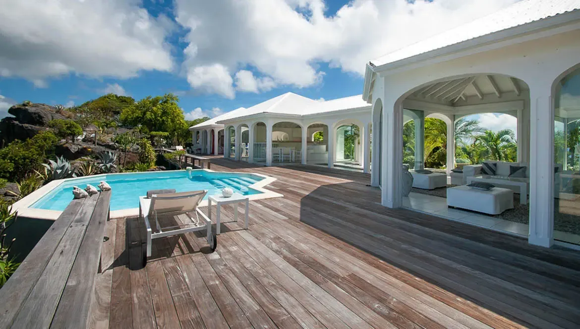 Bask in the Caribbean sun on Villa Byzance's expansive wooden deck, where a turquoise pool invites leisurely dips and panoramic ocean views stretch to the horizon. This St. Barths retreat merges luxury with nature, offering a serene escape amid lush tropical landscaping and elegant open-air living spaces.                                                                                                                                                                                                                 +
 