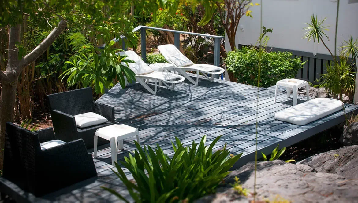 Step onto the private wooden terrace of Villa Byzance, where white sun loungers and plush black wicker seating blend seamlessly with vibrant tropical greenery. This tranquil St. Barths retreat invites you to unwind in style, surrounded by the island's natural beauty and gentle sea breezes.                                                                                                                                                                                                                       +
 