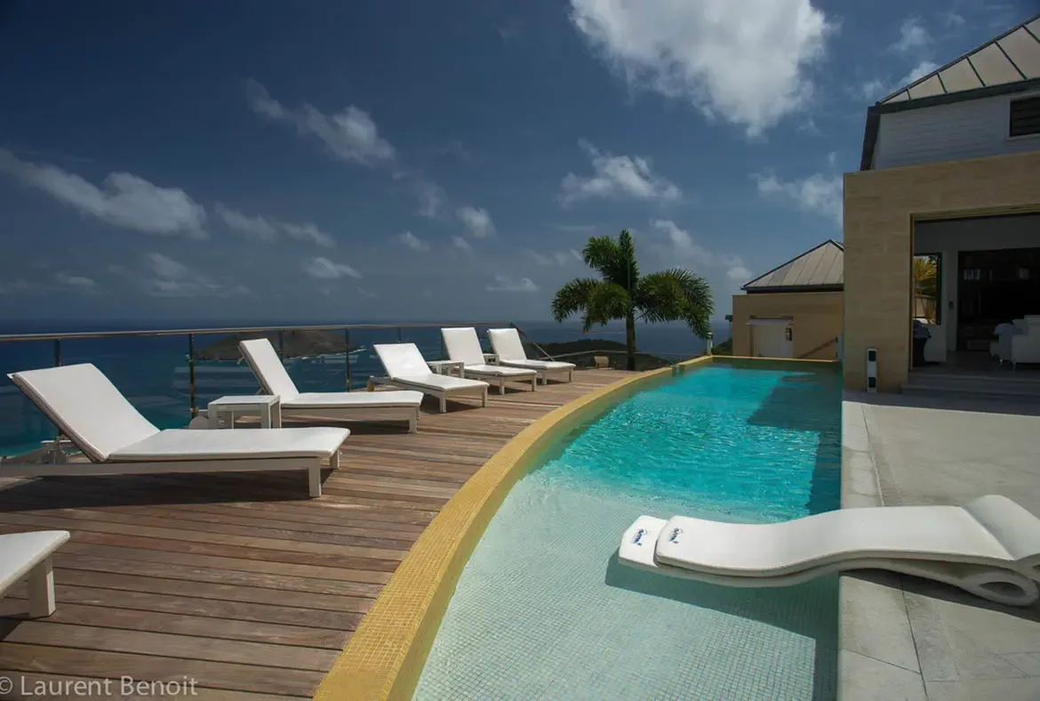 Submerged loungers on the shallow sun shelf offer a unique way to stay cool while immersed in Caribbean views. The infinity pool's crystalline waters seem to spill into the sea, framed by a glass railing that keeps the panorama uninterrupted.