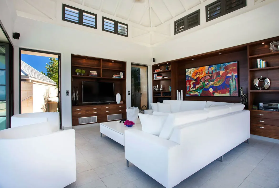 Soaring vaulted ceilings create a cathedral-like atmosphere in this designer living space. Rich dark-wood cabinetry contrasts with white floors, while a vibrant contemporary painting adds gallery-worthy personality to your Caribbean retreat.