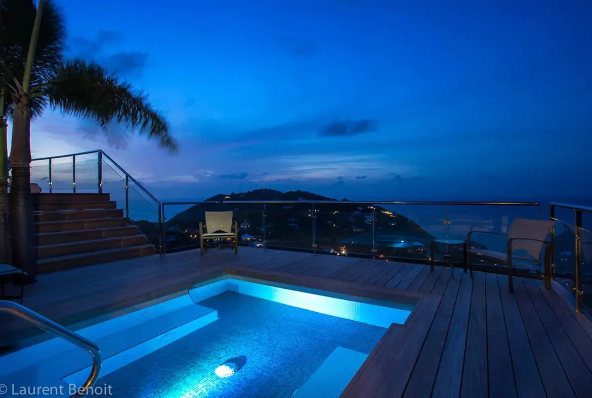 Let the glowing sapphire plunge pool become your evening sanctuary at Villa Donato. Glass railings and warm wood decking frame panoramic views of the Caribbean coastline, where distant harbor lights twinkle beneath the velvety sky.