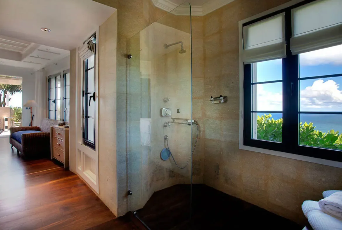Bathe with panoramic views of the turquoise horizon in this glass-enclosed walk-in shower wrapped in textured stone. Polished hardwood floors flow from the spa-like bathroom to an intimate lounge space, where the sea is your constant companion.