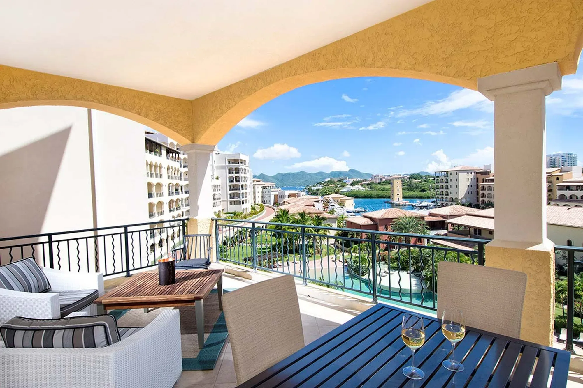 A private terrace unfolds beneath arched colonnades — navy slatted dining and woven loungers poised above a crystalline Caribbean bay.
