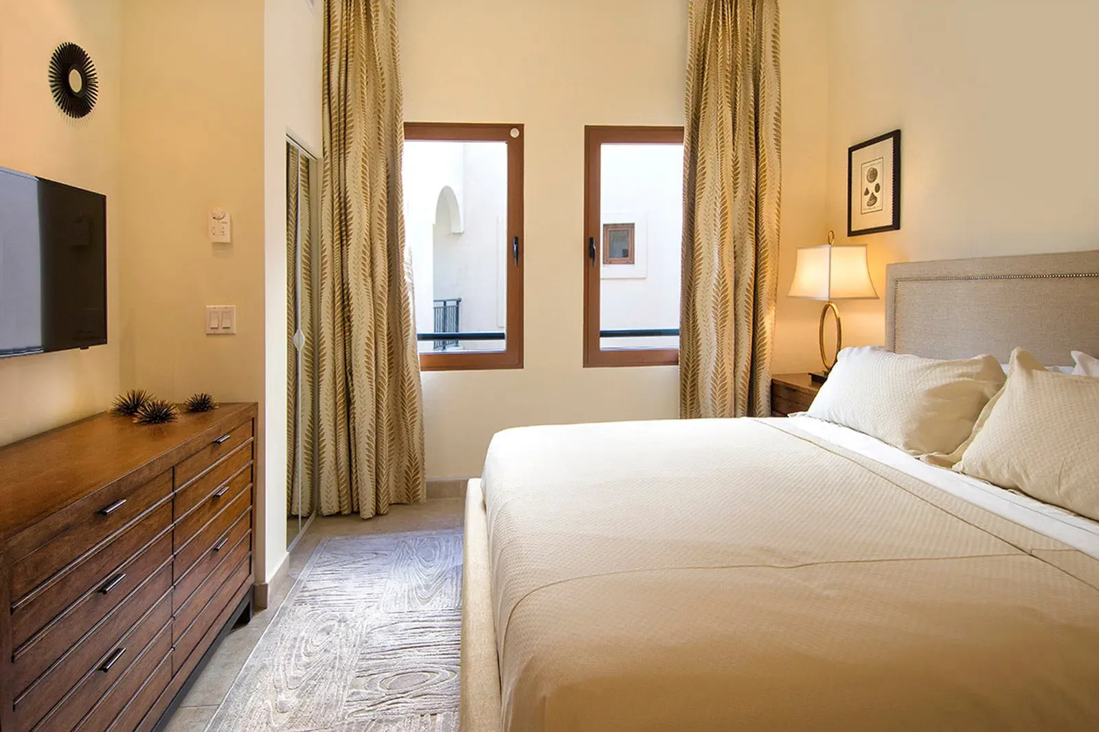 A teal velvet tufted headboard and chevron linens anchor a coastal bedroom suite, where palm-leaf ceiling fans and sage drapes complete the tropical retreat.