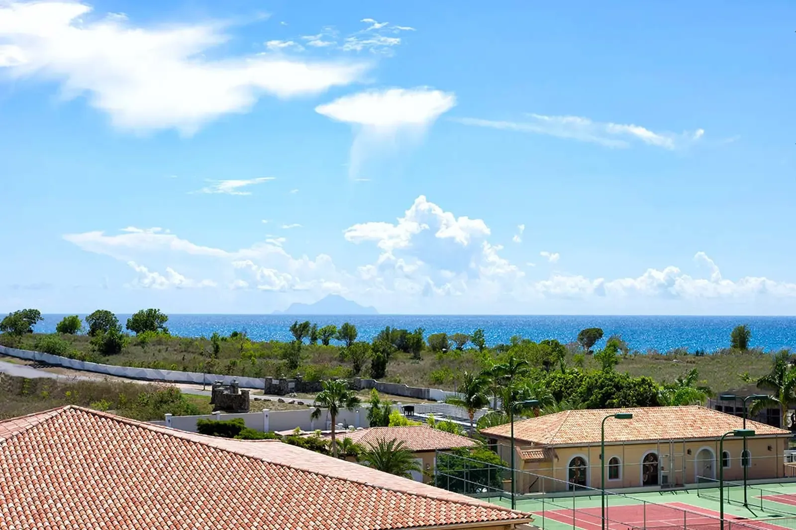 Terracotta rooftops and mature palms frame a resort-style estate, where red clay tennis courts and emerald landscaping speak to a life of refined leisure.