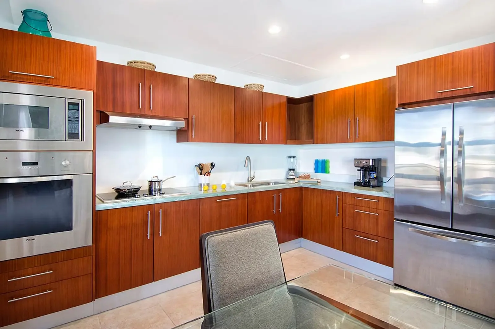 Seafoam marble countertops catch the light above gleaming stainless steel appliances, while horizontal wood grain cabinetry brings warmth to a pristine culinary space.