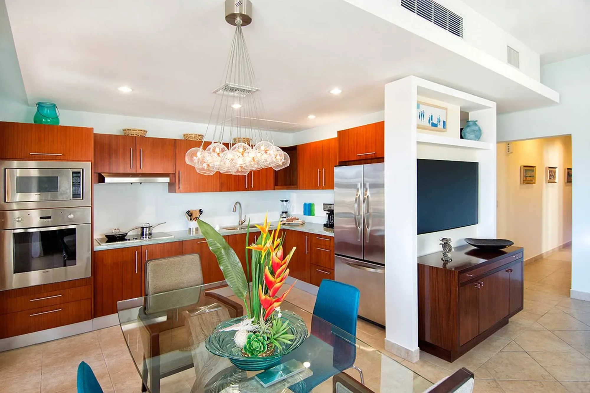A gourmet kitchen in rich warm wood meets open-concept living — where integrated appliances and a cascading glass chandelier define effortless elegance.