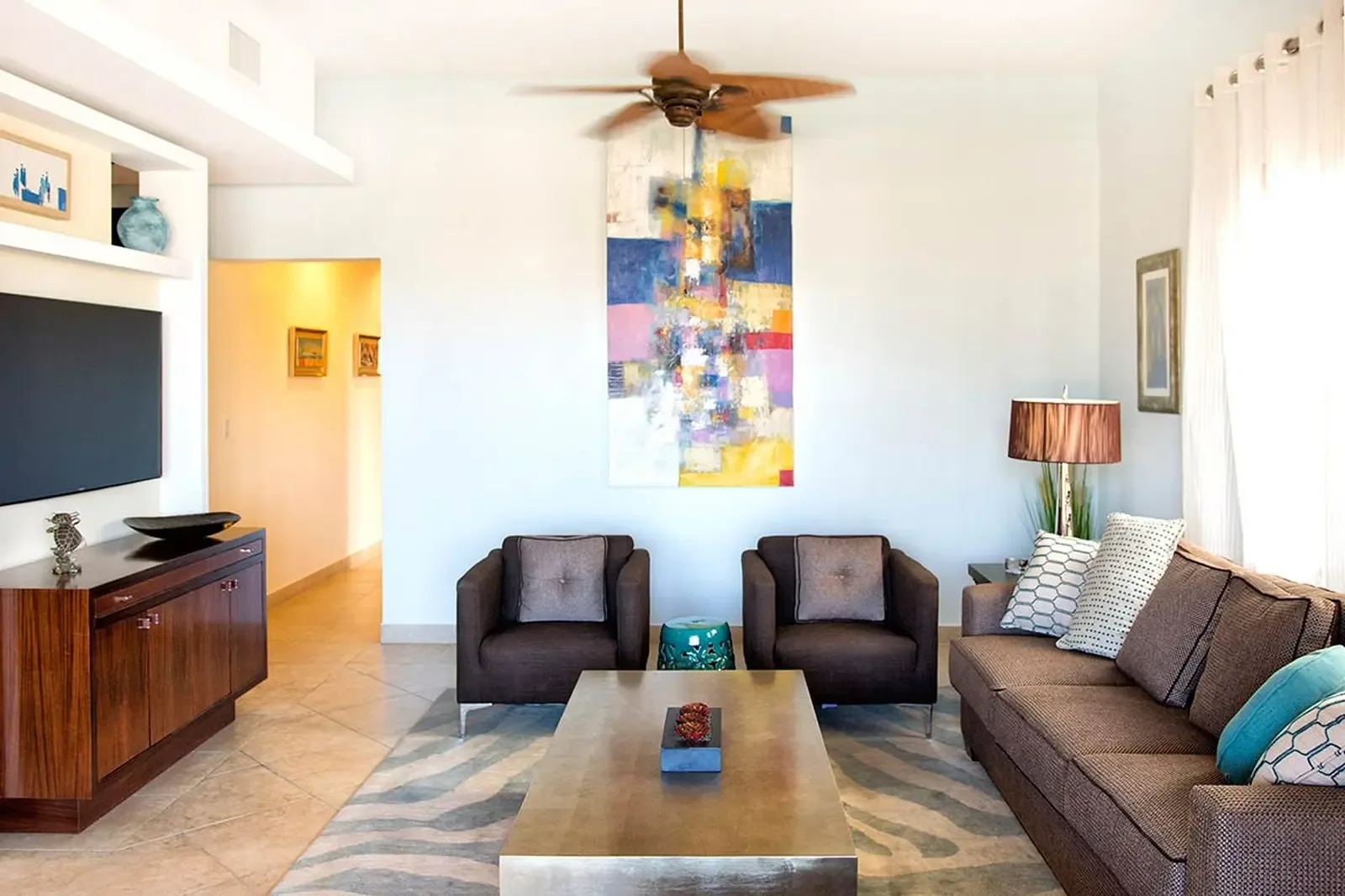 Floor-to-ceiling glass dissolves the boundary between interior and exterior, flooding a sunlit living room with tropical light and garden views.