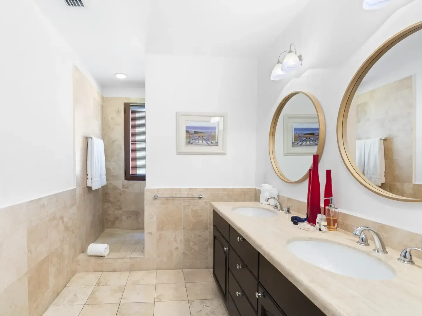 Spa-like master bathroom with a dark wood double vanity, marble countertop, walk-in shower, and beach-scene artwork.