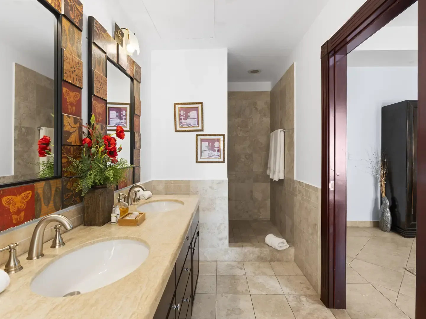 Elegant powder room with a dark wood vanity, decorative tile mirror frame, and vibrant red floral arrangements.