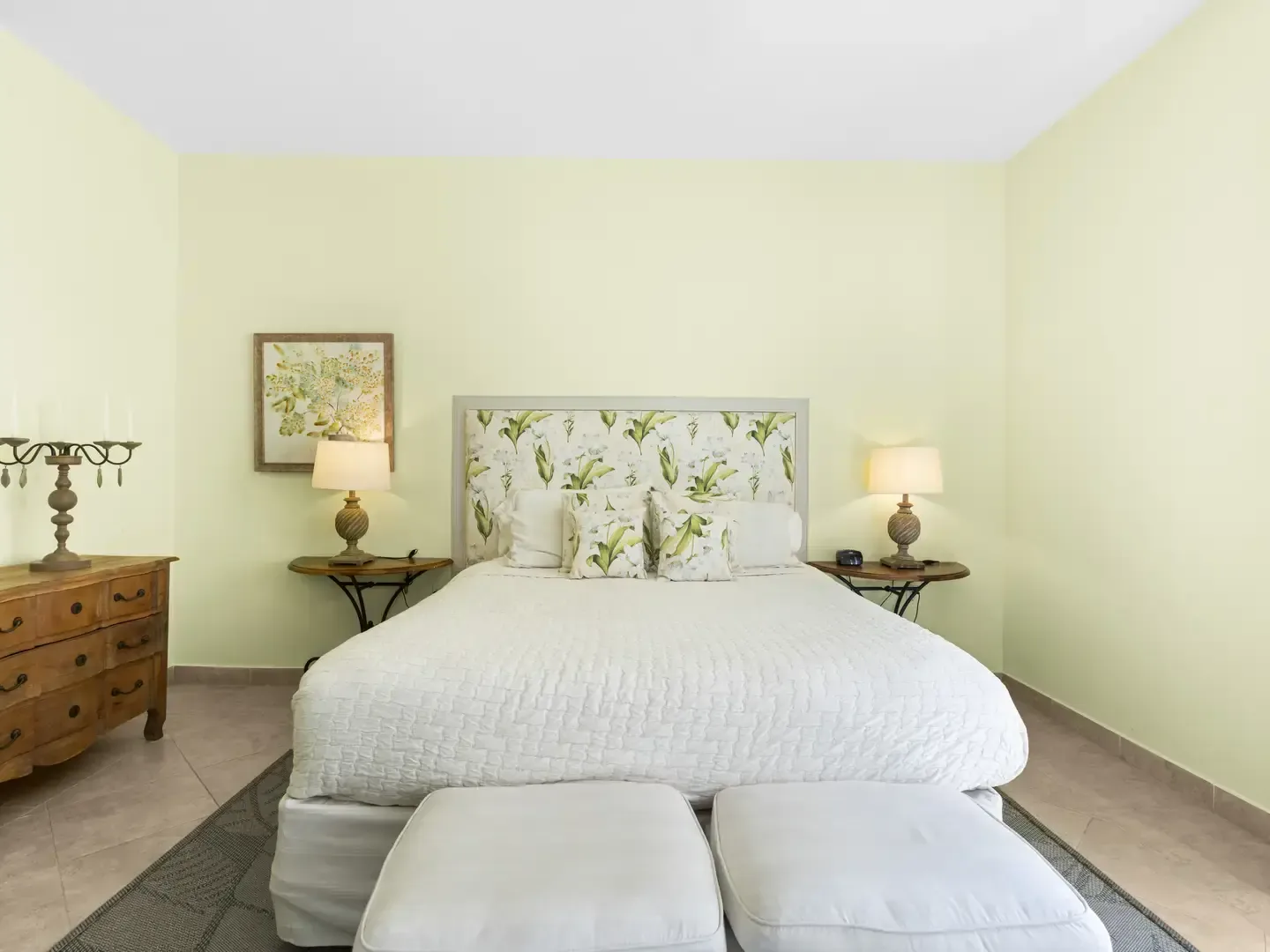Fresh botanical bedroom with a green leaf-patterned headboard, matching curtains, cream upholstered benches, and ocean views.