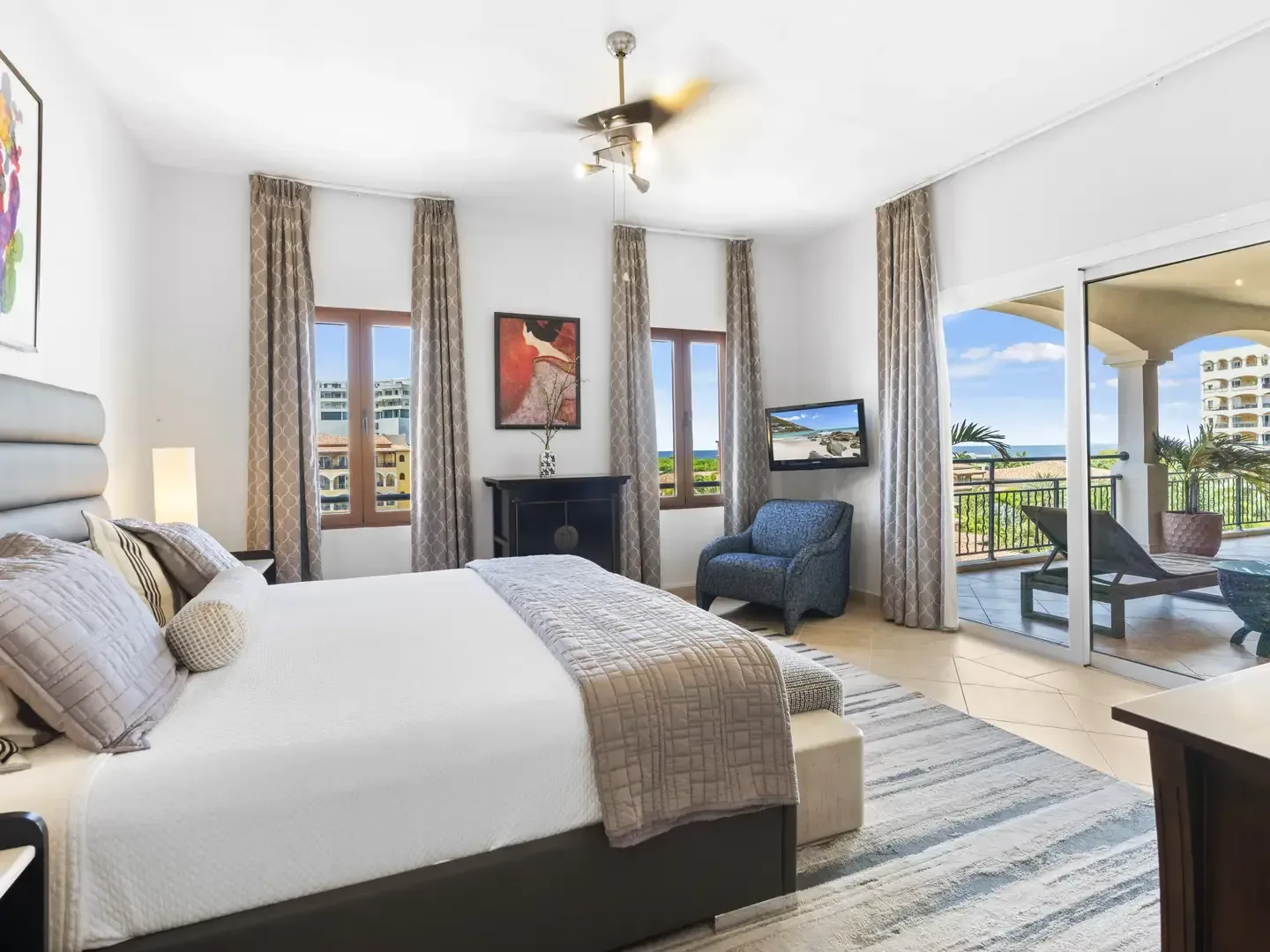 Sophisticated master bedroom with a charcoal grey tufted headboard, abstract art, and a textured grey area rug on light tile floors.