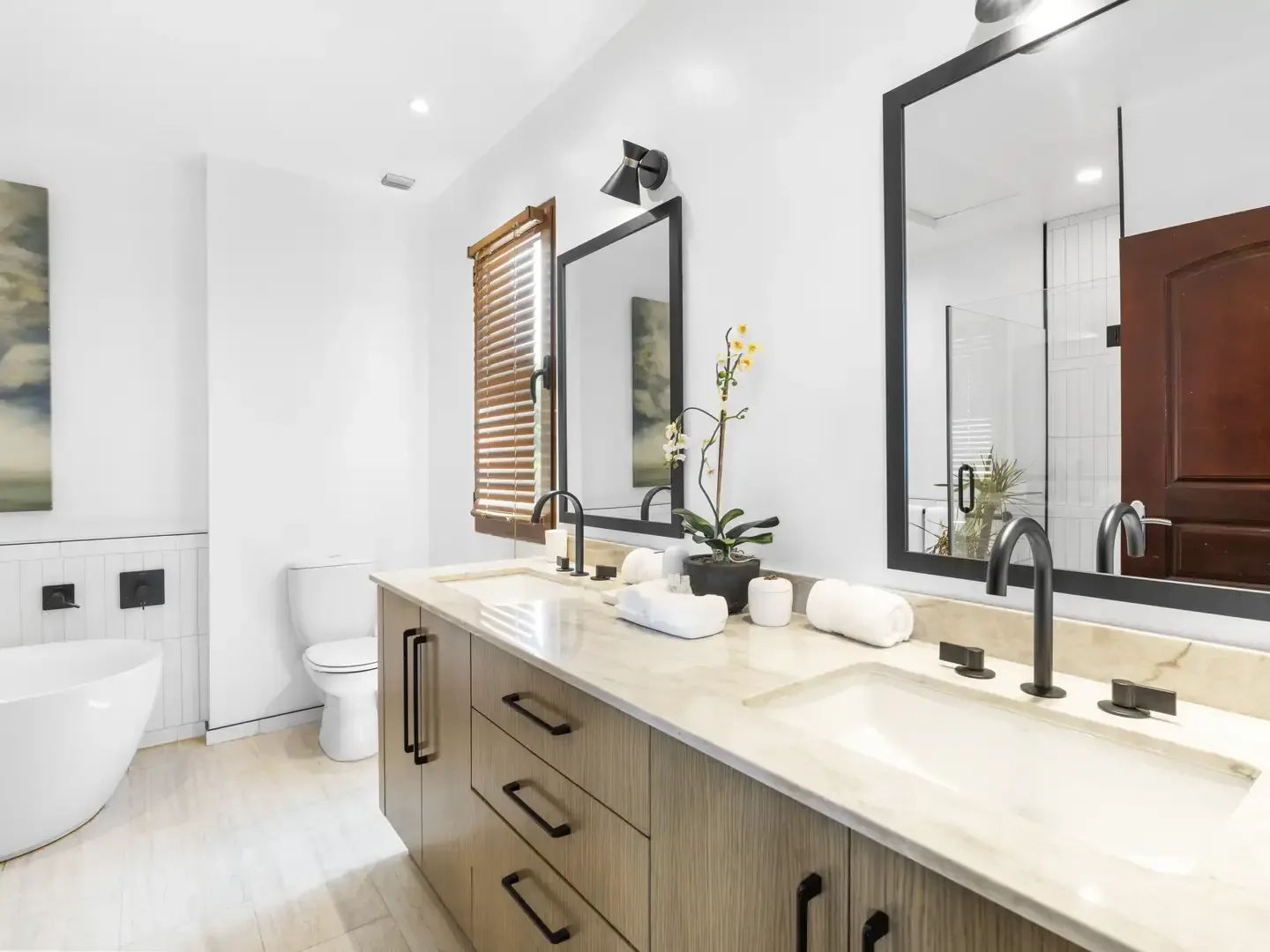 Bright bedroom with a grey upholstered headboard and an open doorway revealing the en-suite bathroom with a double vanity.