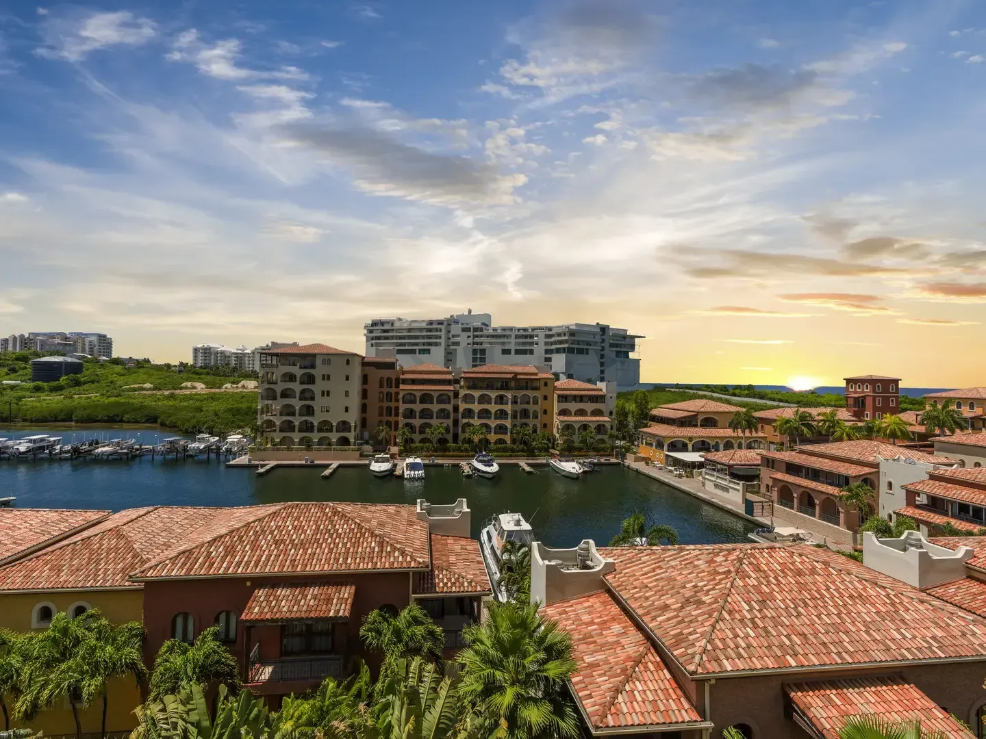 Panoramic aerial view at golden hour overlooking the Porto Cupecoy marina filled with yachts, Mediterranean rooftops, and the blue Caribbean Sea.