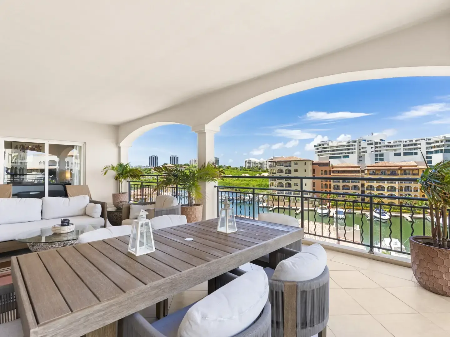 Expansive outdoor terrace with a dark wood dining table and white lounge furniture, overlooking the marina and Caribbean horizon.