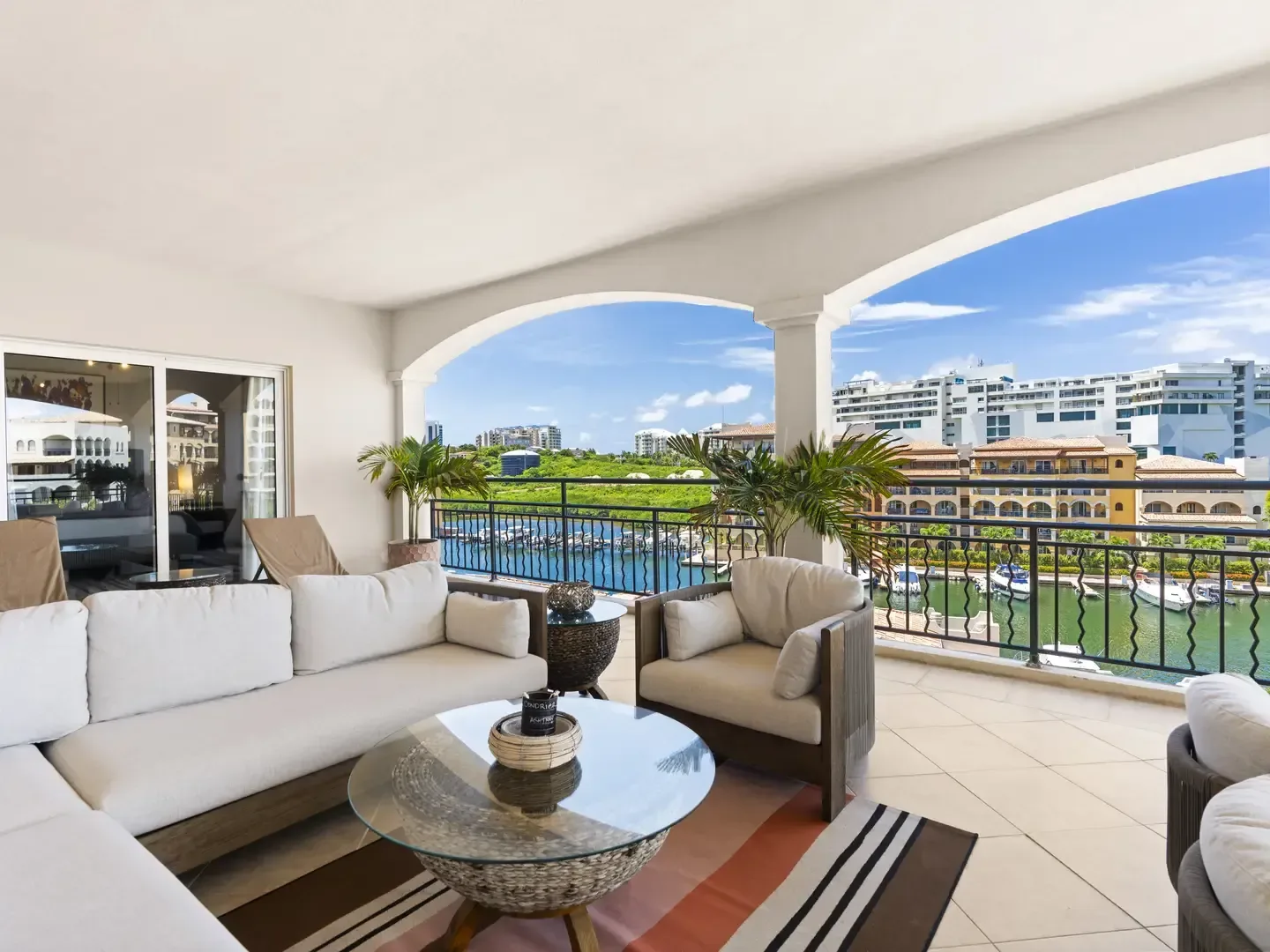 Open terrace styled as an outdoor living room with a sectional sofa, glass coffee table, and a striped rug overlooking the Porto Cupecoy marina.