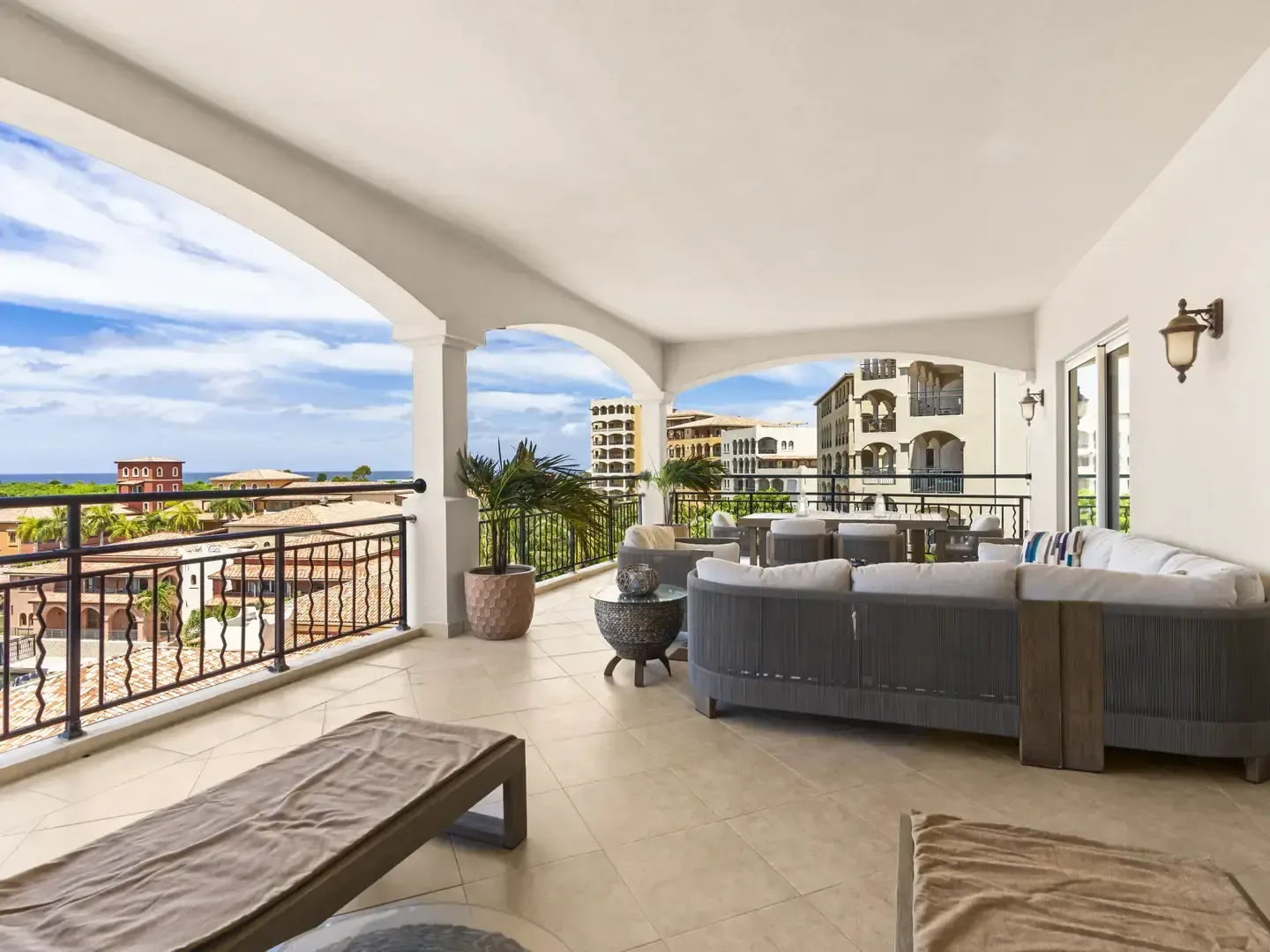 Luxurious covered terrace furnished with a curved sectional and armchairs, offering sweeping views of the Caribbean Sea and resort landscape.