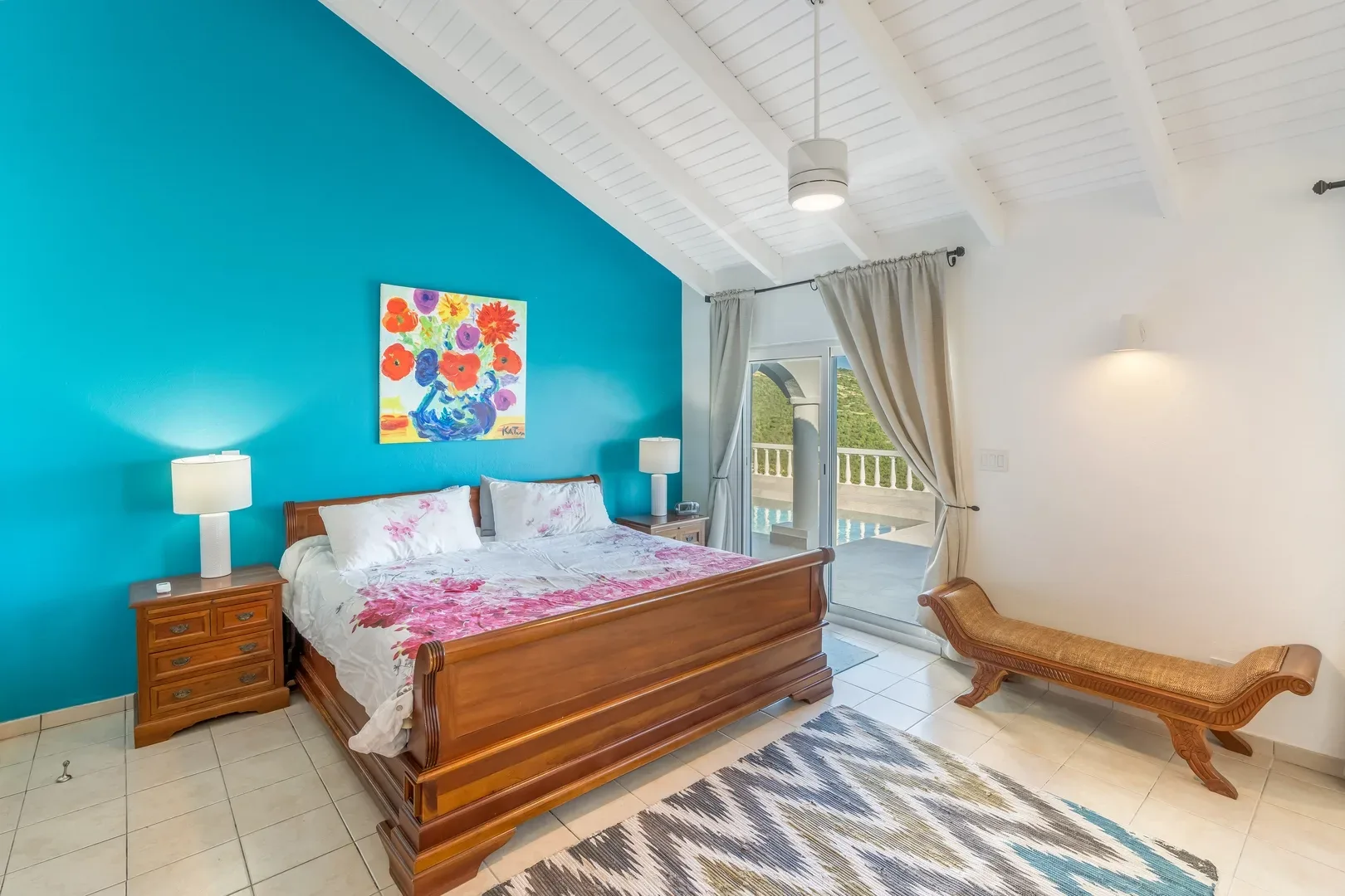 Master bedroom with wooden sleigh bed, turquoise accent wall, colorful floral artwork, and pool view through sliding glass doors