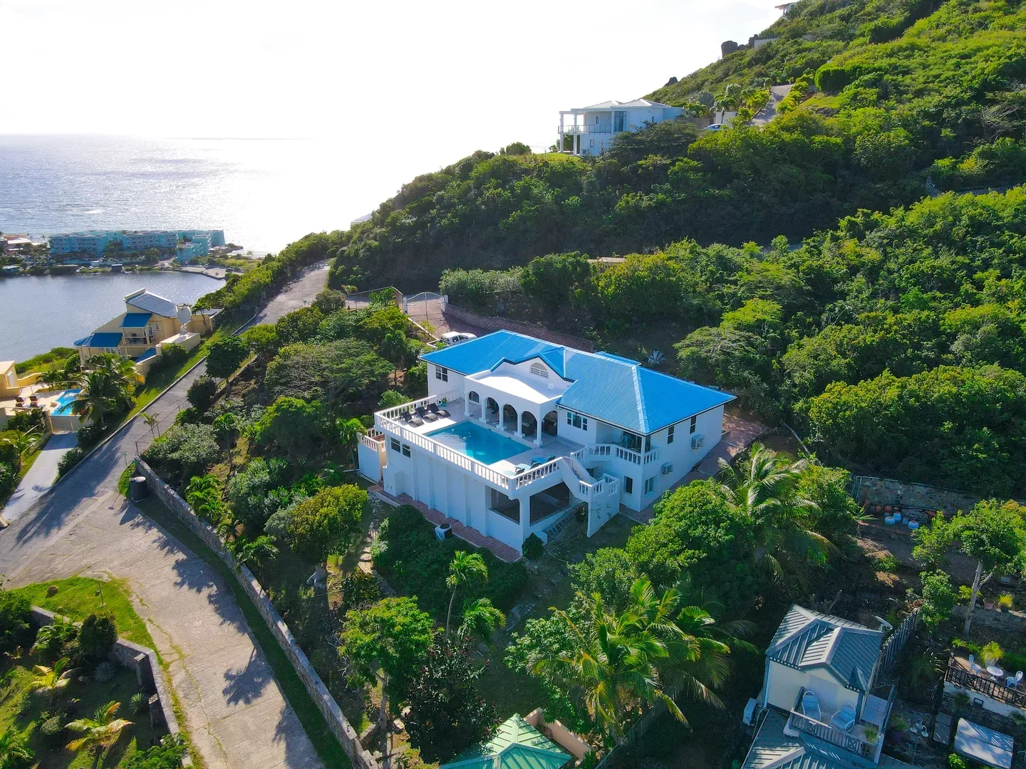 Aerial view of a white luxury villa with a blue roof and private pool on a hillside in St. Maarten, surrounded by tropical greenery and overlooking the ocean