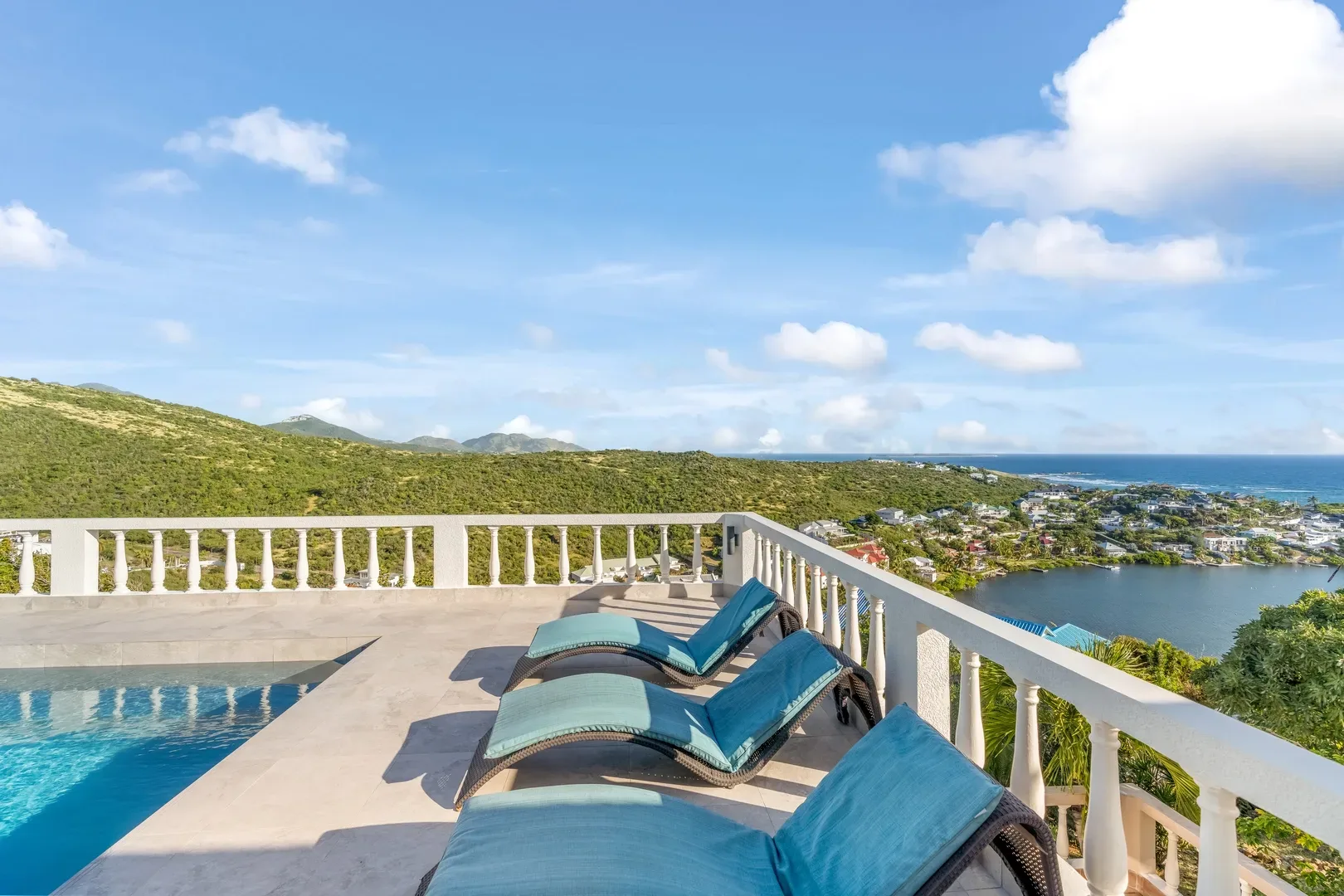 St. Maarten luxury villa terrace with turquoise lounge chairs, swimming pool, and panoramic ocean, mountain, and coastal town view