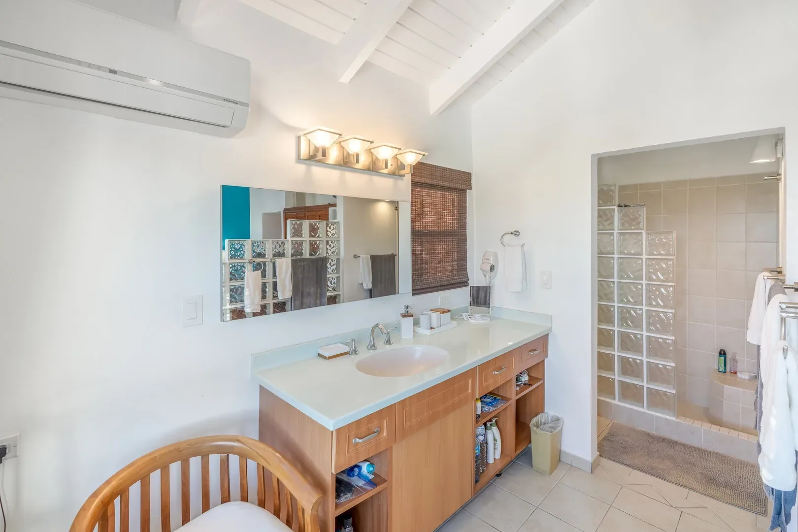 Modern bathroom with wooden vanity, blue countertop, glass block shower, and bamboo window blind
