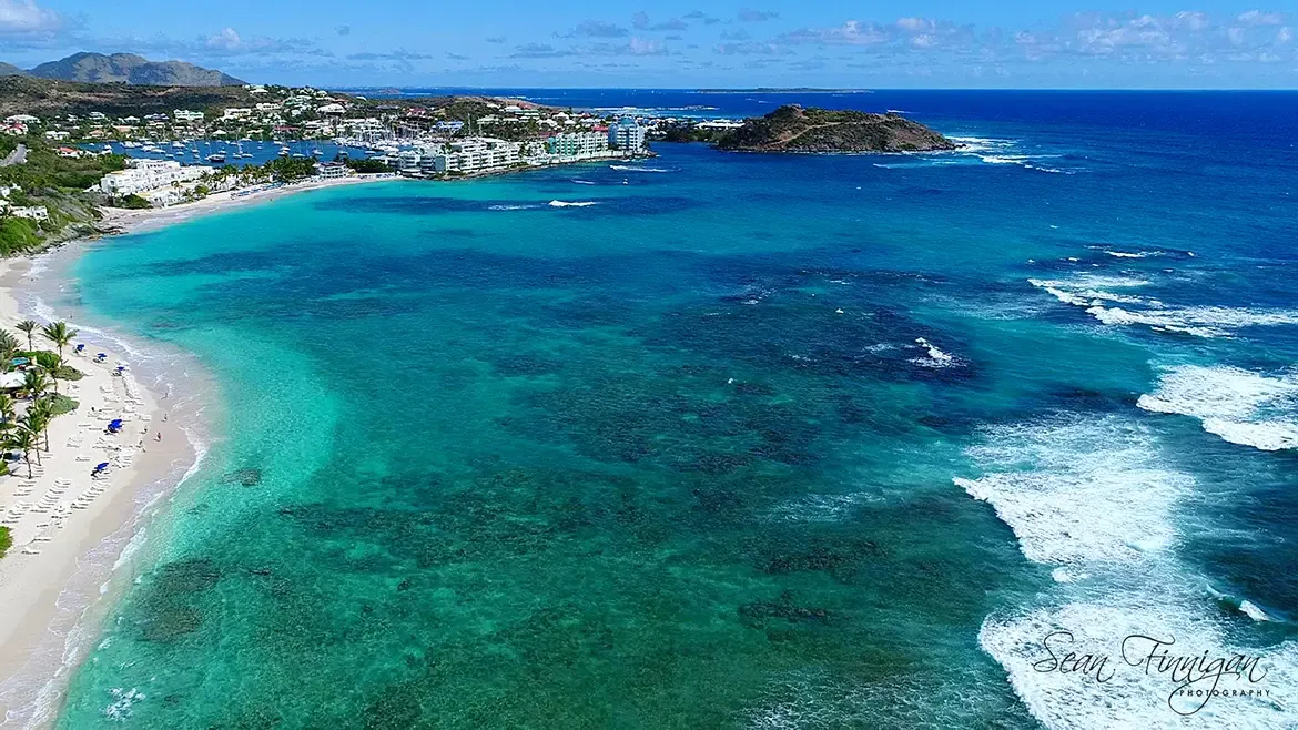 The full resort experience — marina, boats, palm-lined beaches, and hills beyond.