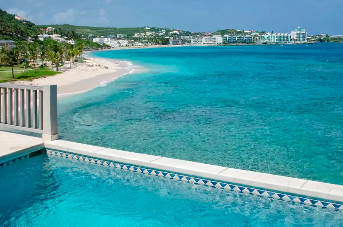 Breathtaking aerial perspective of your beachfront paradise with pool, palm trees, and crystal waters.