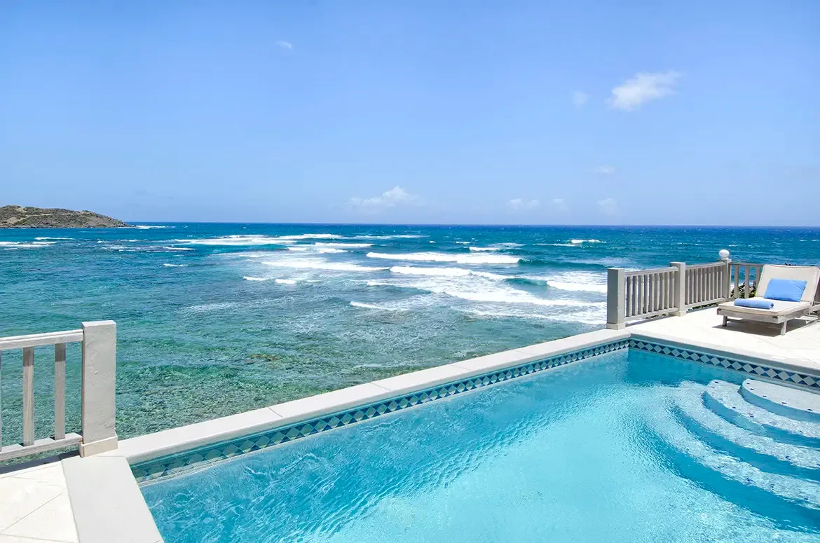Soak up the sun beside the pristine pool with handcrafted blue-white geometric tiles and ocean backdrop.