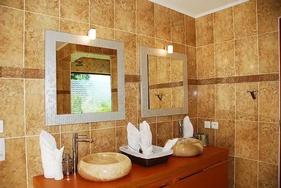 Dual vessel sinks on a wooden vanity with matching square mirrors and warm-toned wall tiling create an elegant bathroom design.